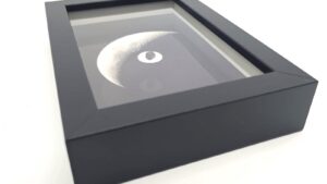 Schwarzer, reliefartiger Rahmen, der ein Foto des Mondes und ein Meteoritenfragment enthält